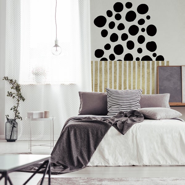 Modernes Schlafzimmer mit gemusterten Kissen auf dem Bett und einer Wandgestaltung aus schwarzen Punkten und goldfarbenen vertikalen Streifen.