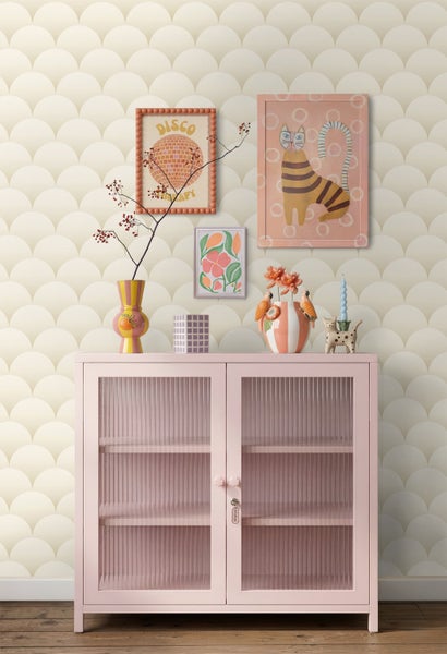 Tapete mit Schuppenmuster an einer Wand hinter einer rosa Kommode mit geriffeltem Glas und verschiedenen Dekorationsartikeln.
