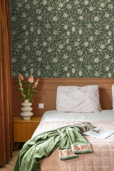 Dekorative Szene mit Koffern, Getränkeflaschen, Kerzen und Gläsern vor einer floral gemusterten Tapete