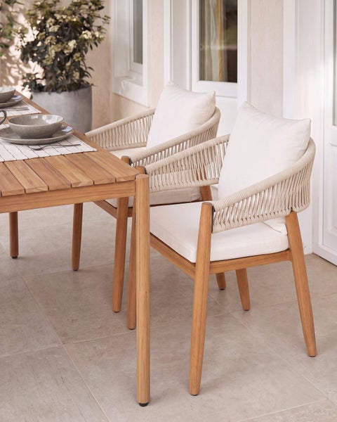 Gartenessgruppe mit Holztisch und zwei Stühlen aus Holz mit geflochtener Rückenlehne und Sitzkissen auf einer Terrasse.