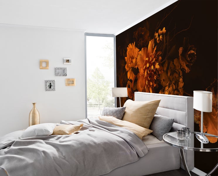 Fototapete mit großen orangefarbenen Blumen auf dunklem Hintergrund in einem modern eingerichteten Schlafzimmer mit weißem Polsterbett.