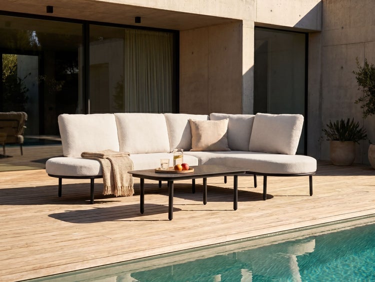 Moderne Garten-Lounge-Garnitur auf einer Holzterrasse am Pool, bestehend aus einem weißen Ecksofa und einem schwarzen Couchtisch.