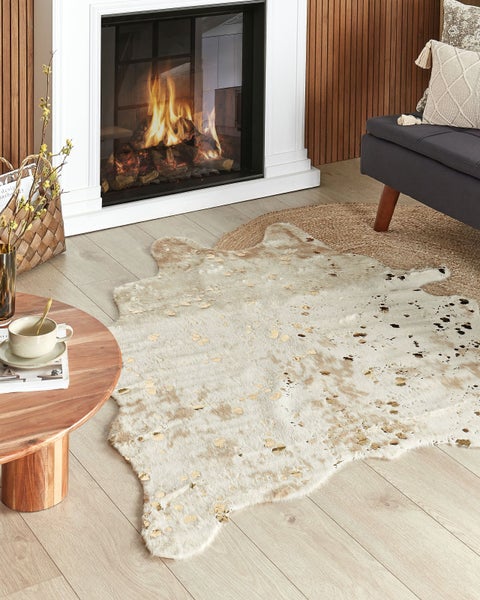 Wohnzimmer mit Kamin, Kunstfellteppich in Tierfelloptik auf hellem Holzboden, runder Holztisch und Sofa in einem modern eingerichteten Raum.