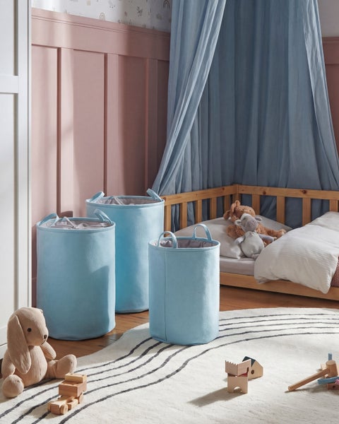 Drei Aufbewahrungskörbe aus hellblauem Filz in verschiedenen Größen in einem Kinderzimmer mit Holzbett, Teppich und Spielzeug.