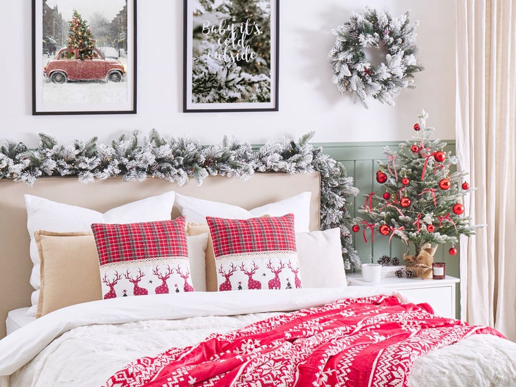 Weihnachtlich dekoriertes Schlafzimmer mit Bett, Kissen, Decke, Girlande, Kranz und kleinem Tannenbaum