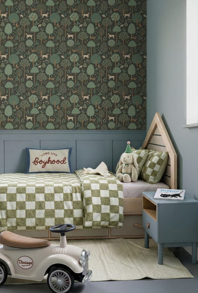 Gemütliches Kinderzimmer mit Waldmotiv-Tapete, einem hölzernen Hausbett, karierter Bettwäsche und einem Retro-Rutschauto vor blau-grauer Wandpaneele.