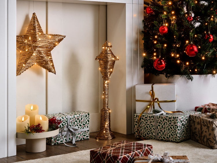 Festliche Szene mit Sternenleuchte, Laterne und Geschenken neben einem Weihnachtsbaum.