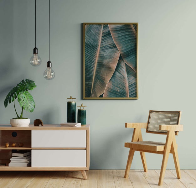 Modern eingerichteter Wohnraum mit gerahmtem Bild von Palmenblättern, Hängeleuchten, Sideboard aus Holz, Monstera-Pflanze und Holzstuhl.