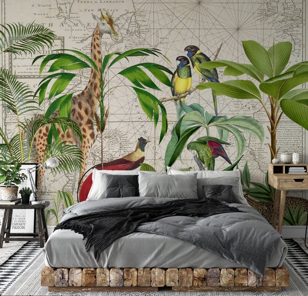 Schlafzimmer mit Vliestapete mit Motiven einer Vintage-Weltkarte, Giraffe, Papageien und tropischen Blättern hinter einem Bett mit Holzrahmen.