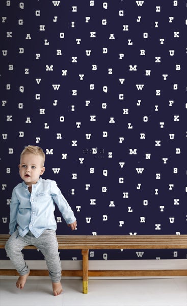 Ein Kind sitzt vor einer Wand mit Buchstabenmuster.