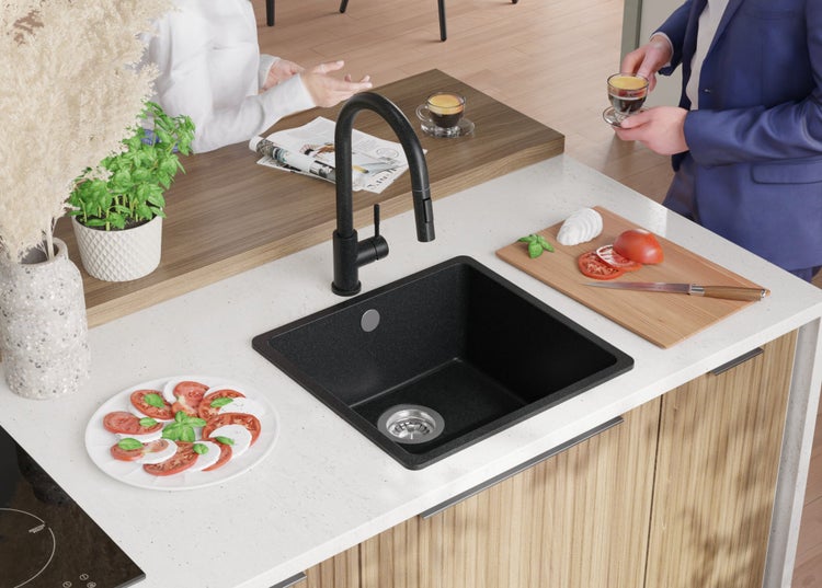 Schwarzes Küchenspülbecken mit Armatur auf einer Küchentheke mit Speisen