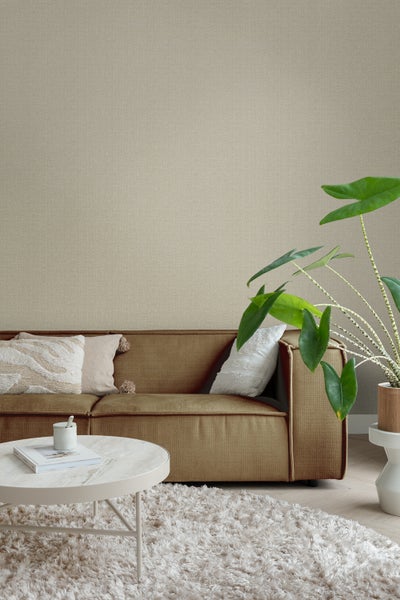 Wohnzimmer mit beiger Textiltapete, Sofa, Tisch, Teppich und Zimmerpflanze für eine gemütliche Atmosphäre.