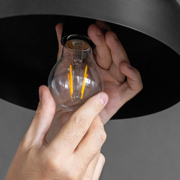 Eine Person schraubt eine klare LED-Lampe in eine schwarze Lampenfassung.