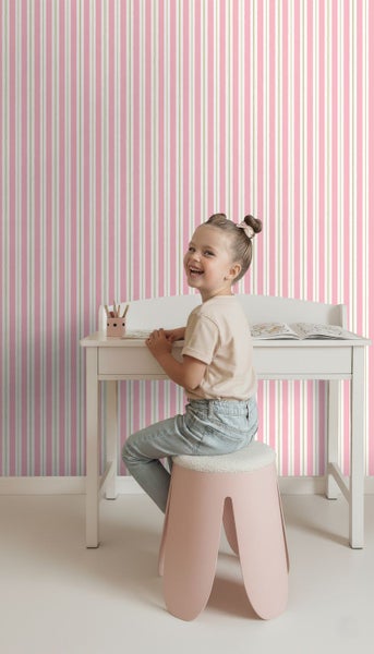 Mädchen sitzt an einem Schreibtisch vor einer gestreiften Tapete