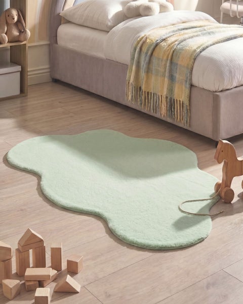 Weicher, wolkenförmiger Kinderteppich in Hellgrün in einem hellen Kinderzimmer mit Holzspielzeug und Bett.
