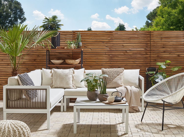 Gartenszene mit Loungesofa, Tisch, Stuhl und Holzzaun im Hintergrund