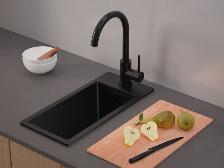 Moderne schwarze Küchenspüle mit schwarzer Armatur auf grauer Arbeitsplatte neben einem Holzschneidebrett mit Birnen.