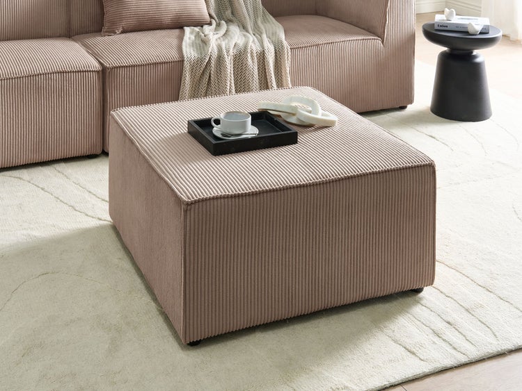 Quadratischer Hocker aus Cord-Stoff in einem modern eingerichteten Wohnzimmer auf einem hellen Teppich.