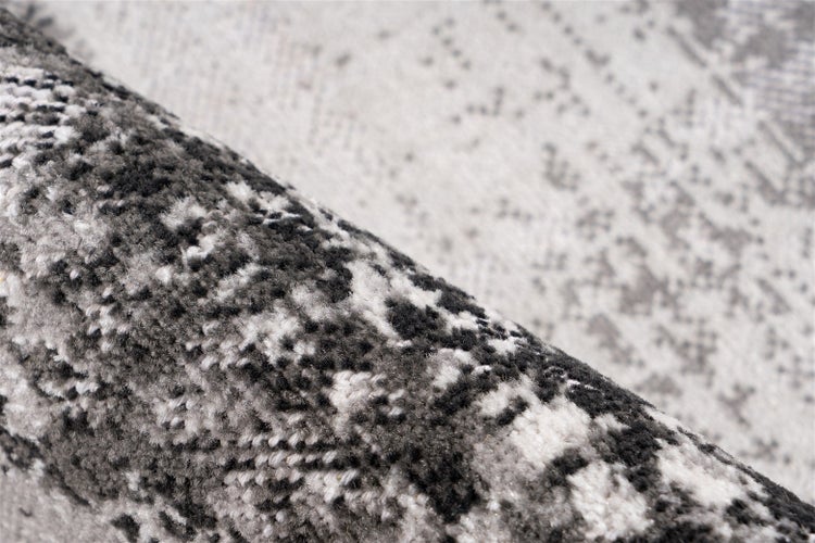 Detailansicht eines Teppichs mit abstraktem Muster in Grau und Weiß, weicher Flor.