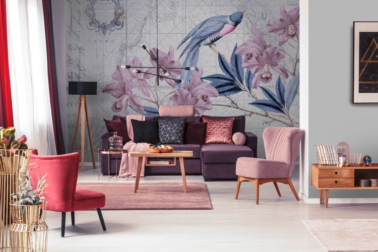 Modernes Wohnzimmer mit Fototapete mit Vogel- und Blumenmotiv auf Weltkarte, lila Sofa, rosa Sessel, Holzmöbeln und modernen Leuchten.