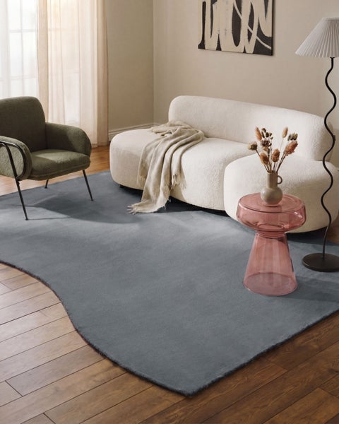 Großer grauer Teppich mit unregelmäßiger Wellenform in einem hellen, modernen Wohnzimmer mit weißem Sofa und Holzfußboden.