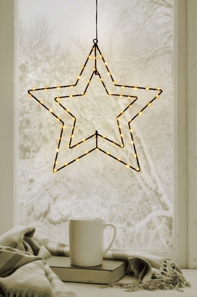 Dekorativer Fensterbereich mit einem beleuchteten Stern, einer Tasse und einer Decke für eine gemütliche Atmosphäre.
