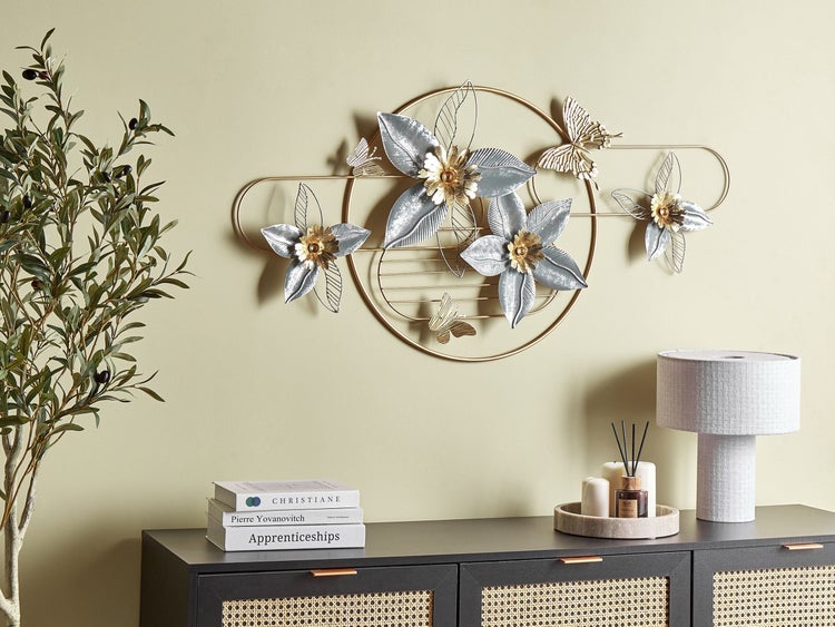 Dekorative Metallwandkunst mit Blumen- und Schmetterlingsmotiven über einer Kommode mit Lampe und Büchern