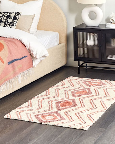 Rechteckiger Teppich mit geometrischem Rautenmuster im modernen Schlafzimmer neben einem gepolsterten Bett und schwarzem Metallschrank.