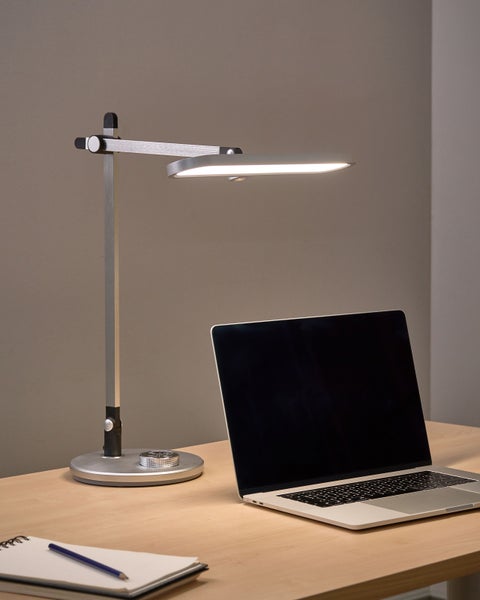 Moderne Schreibtischleuchte aus Metall neben einem Laptop auf einem Tisch