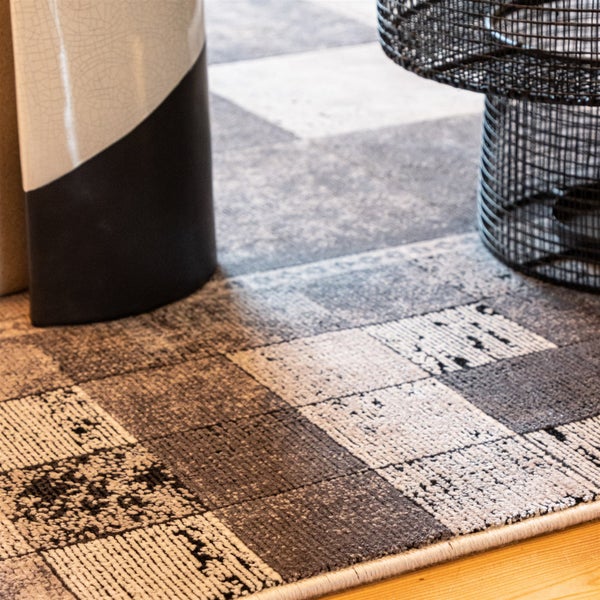 Kurzflor-Teppich mit Karomuster und Patchwork-Design auf Holzboden neben einem Beistelltisch aus Drahtgeflecht.