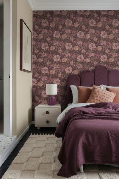 Schlafzimmer mit gemusterter Tapete, Bett, Nachttisch, Lampe und Teppich