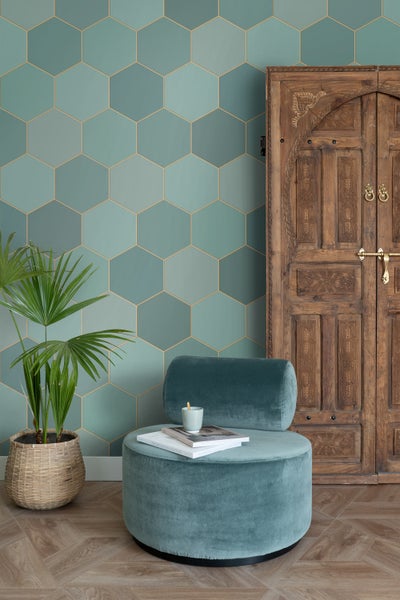 Helles Zimmer mit türkisfarbenen Wandfliesen in Hexagonform, einem Sessel, einer Holztür und einer Topfpflanze