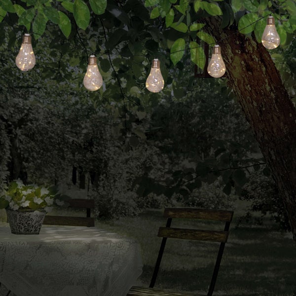 Dekorative Lichterkette mit Glühbirnen, die einen Gartentisch beleuchten.