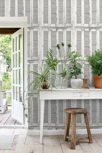 Dekorative Szene mit weißer Konsole, Pflanzen und Fensterladen-Tapete für ein stimmungsvolles Ambiente.