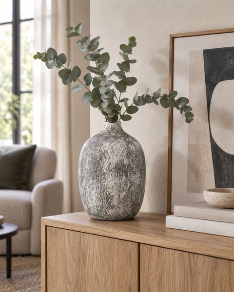 Dekorative Vase mit strukturierter Oberfläche auf einem Sideboard aus Holz dekoriert mit Eukalyptuszweigen im Wohnzimmer.