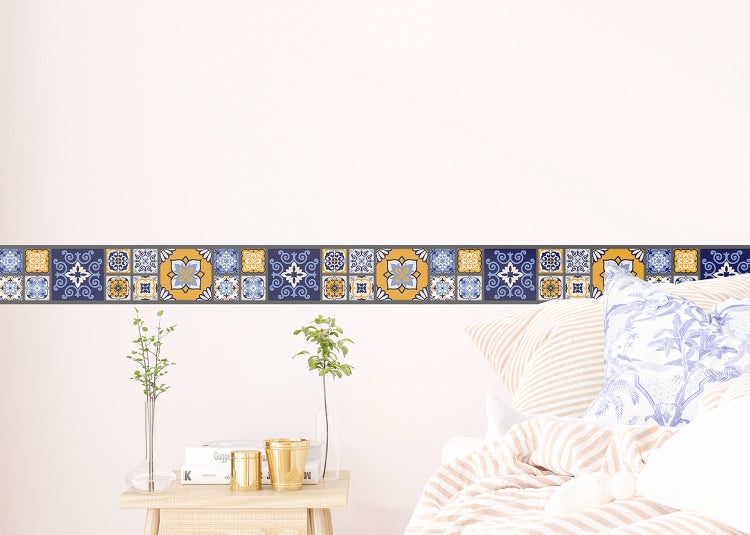 Selbstklebende Tapetenbordüre mit mediterranem Fliesenmuster an einer weißen Wand in einem hellen Schlafzimmer.