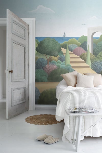 Heller Raum mit Wandbild, Bett, Tisch und offener Tür