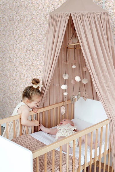 Babyzimmer mit Gitterbett, Baldachin und einem Kind, das über das Bett schaut.