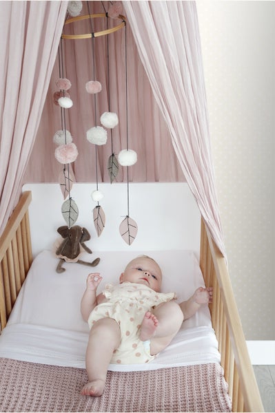 Baby liegt in einem Kinderbett mit Mobile und Betthimmel