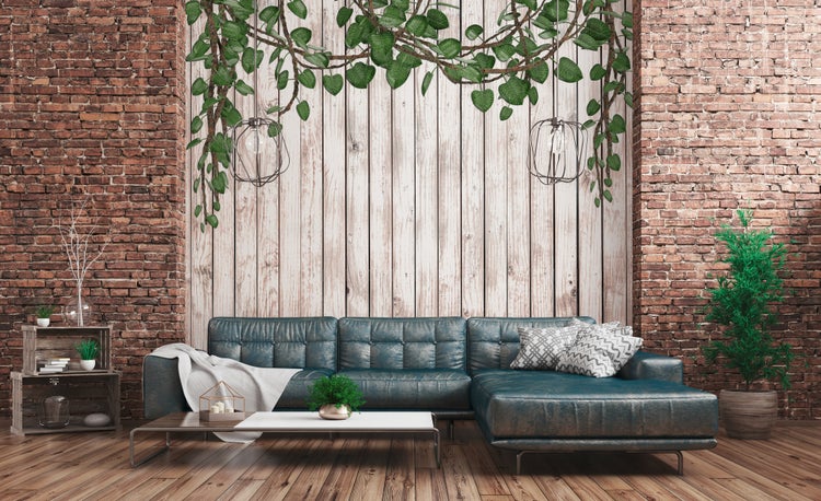 Wohnzimmer mit Sofa, Couchtisch, Zimmerpflanzen, Ziegelwand und Fototapete in Holzoptik mit herabhängenden Pflanzenmotiven.