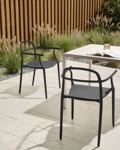 Zwei Armlehnstühle aus Kunststoff im Garten neben einem Tisch.