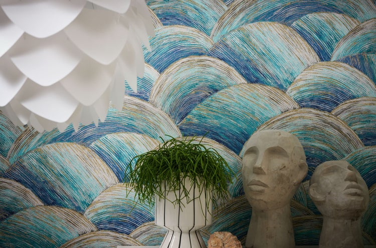 Innenaufnahme eines Wohnzimmers mit einem blauen Sessel, einer Zimmerpflanze und einer gemusterten Tapete