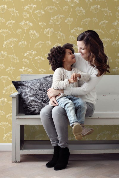 Eine Mutter umarmt ihr Kind auf einer Bank vor einer Wand mit Blumenmustertapete.