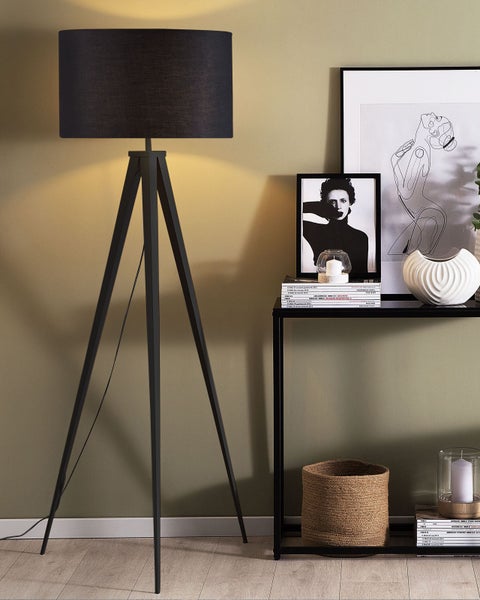 Stehlampe mit schwarzem Lampenschirm auf einem Stativ neben einem Konsolentisch mit Dekorationen