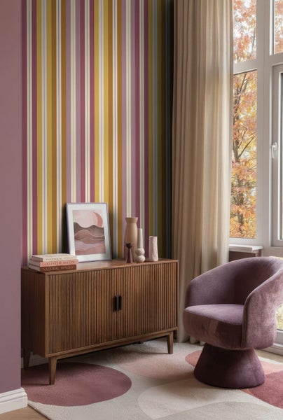 Modernes Wohnzimmer mit vertikal gestreifter Tapete, einem hölzernen Sideboard und einem Sessel auf einem gemusterten Teppich.