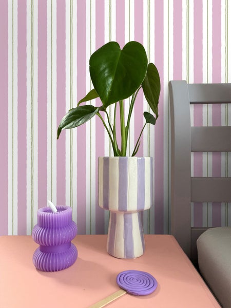 Dekorative Szene mit Pflanze im gestreiften Topf, Kerze und Lutscherstil auf einem Nachttisch