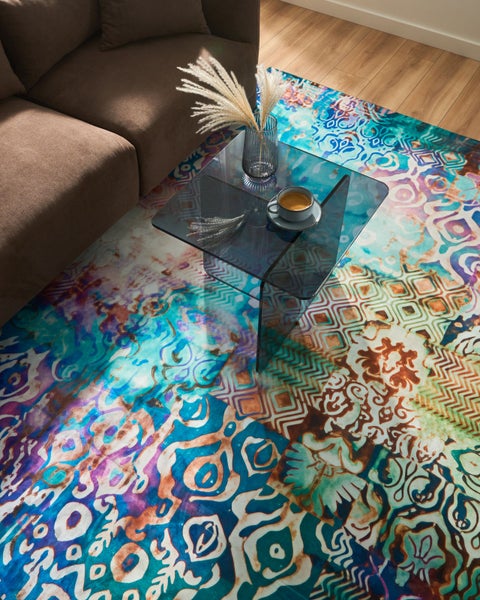 Farbenfroher Teppich im Patchwork-Design mit verschiedenen Mustern unter einem modernen Glastisch im hellen Wohnzimmer.