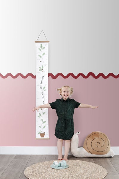 Mädchen vor einer Wachstumstabelle mit Eichenmotiv im Kinderzimmer