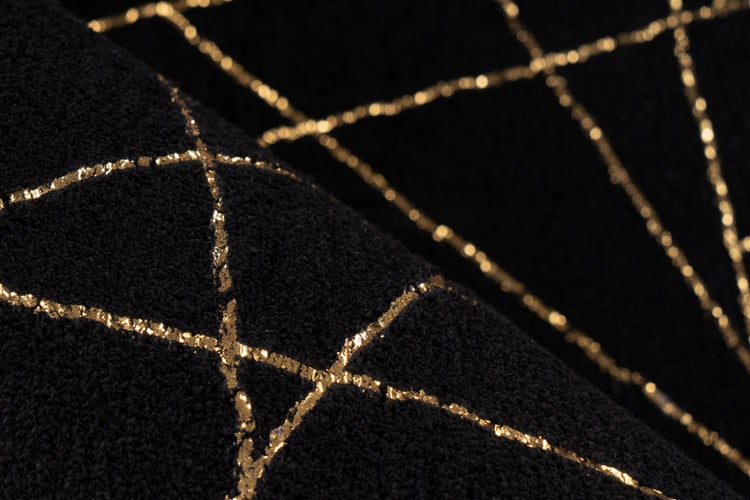 Detailaufnahme eines schwarzen, strukturierten Textils mit einem geometrischen Muster aus goldenen Linien.