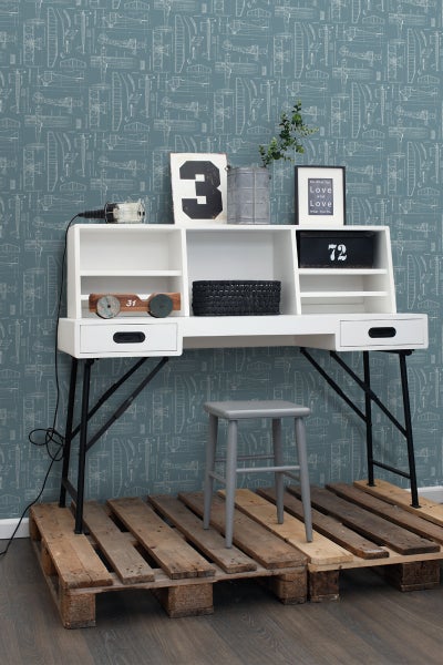 Schreibtisch mit Regalen, Hocker und Dekoration auf Holzpaletten vor einer Wand mit Flugzeugmuster.